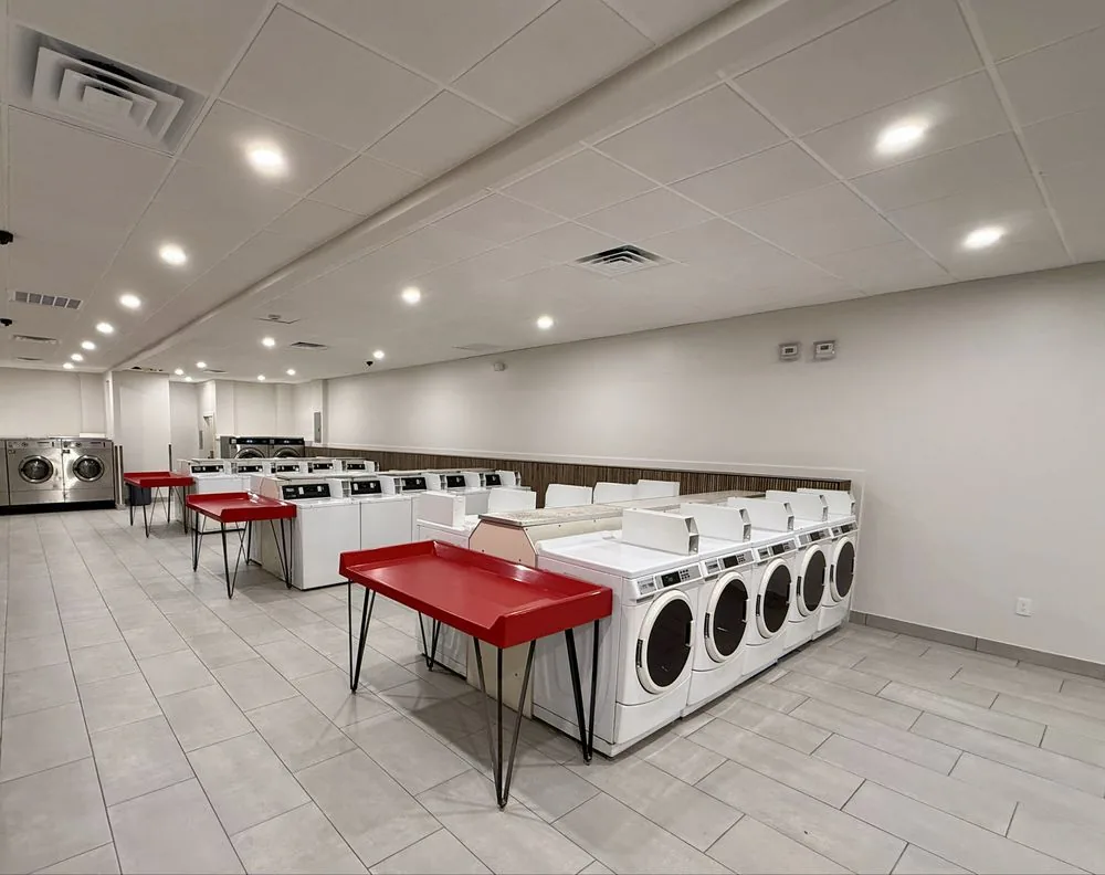 Rows of clean, modern washers and dryers with red folding tables inside Retro Laundry Co.